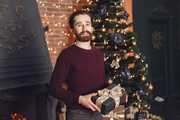 Glücklicher Mann im roten Pullover. Mann vor dem Kamin. Männchen auf dem Hintergrund des Weihnachtsbaumes.