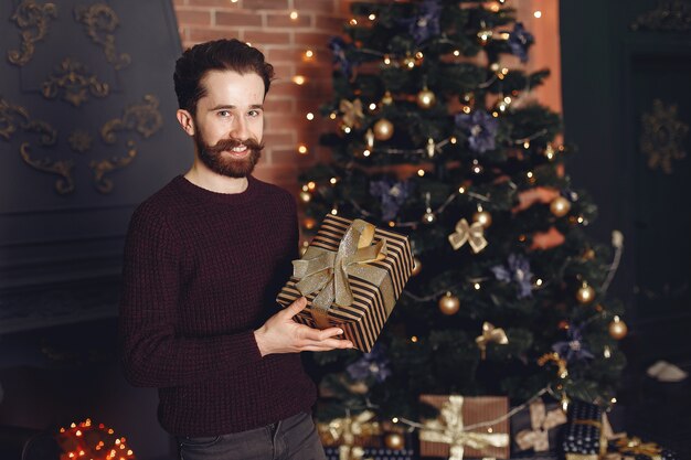 Glücklicher Mann im roten Pullover. Mann vor dem Kamin. Männchen auf dem Hintergrund des Weihnachtsbaumes.