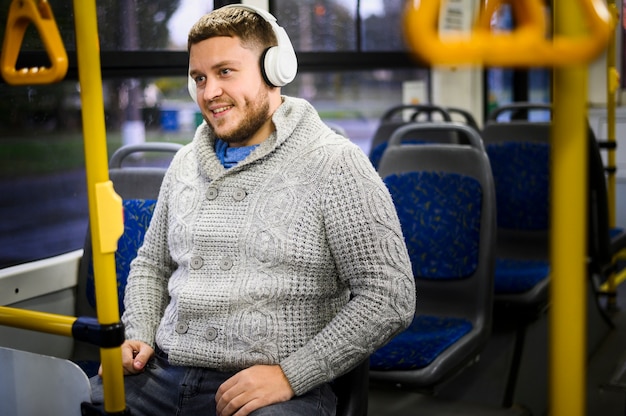 Glücklicher Mann mit den Kopfhörern, die auf einem Bussitz sitzen