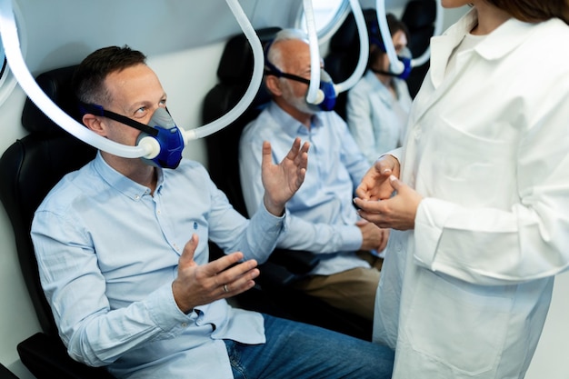 Glücklicher Mann mit Sauerstoffmaske und Gespräch mit einer Ärztin in der Überdruckkammer in der Klinik
