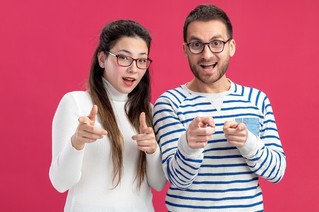 glücklicher Mann und Frau des jungen schönen Paares in der Freizeitkleidung, die die Brille trägt, die glücklich und fröhlich mit Zeigefingern zeigt