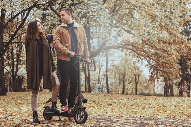 Glücklicher Mann und Frau haben eine schöne Fahrt mit dem Roller im goldenen Herbstpark.