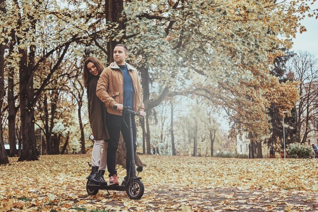 Glücklicher Mann und Frau haben eine schöne Fahrt mit dem Roller im goldenen Herbstpark.