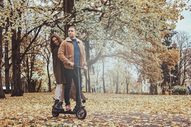 Glücklicher Mann und Frau haben eine schöne Fahrt mit dem Roller im goldenen Herbstpark.