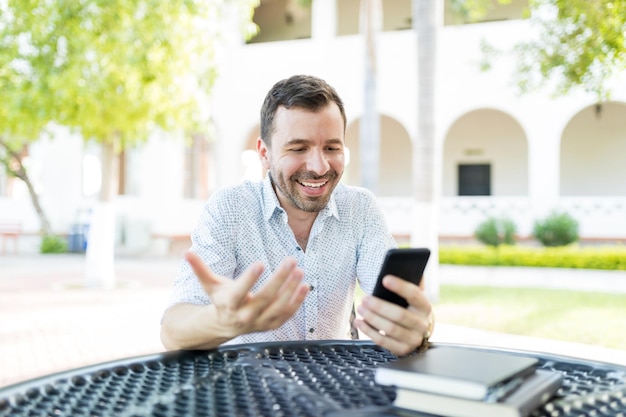 Glücklicher mittlerer erwachsener Mann, der per Videoanruf per Handy kommuniziert, während er im Garten sitzt