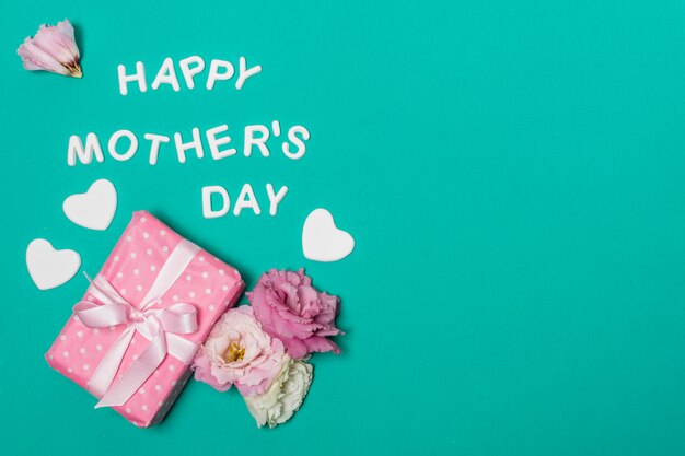 Glücklicher Muttertagstitel nahe Blumen und Geschenkbox