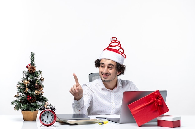 Glücklicher positiver junger Geschäftsmann mit lustigem Weihnachtsmannhut, der zu jemandem im Büro auf weißem Hintergrund spricht