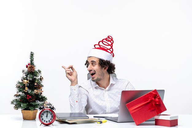 Glücklicher positiver überraschter junger Geschäftsmann mit lustigem Weihnachtsmannhut, der mit jemandem im Büro auf weißem Hintergrund spricht