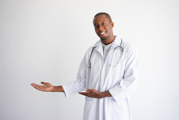 Glücklicher schwarzer männlicher Doktor, der auf leeren Raum zeigt und Produkt darstellt.