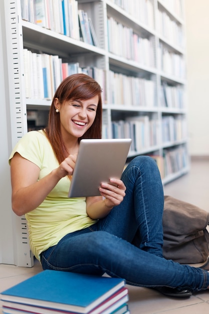 Glücklicher student, der digitales tablett in bibliothek verwendet