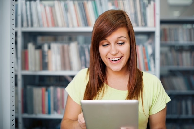 Glücklicher Student, der digitales Tablett in Bibliothek verwendet