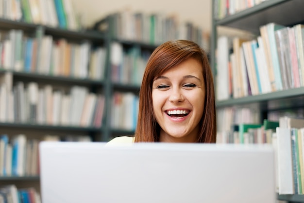 Glücklicher Student, der Laptop in Bibliothek verwendet