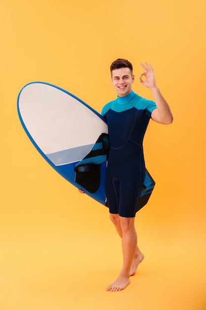 Kostenloses Foto glücklicher surfer, der mit surfbrett geht und ok zeichen zeigt