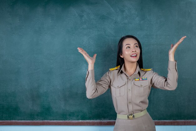 glücklicher thailändischer Lehrer im offiziellen Outfit, der vor dem Rückenbrett handelt