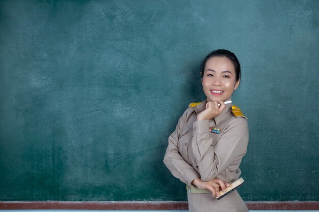 glücklicher thailändischer Lehrer im offiziellen Outfit, der vor Tafel posiert