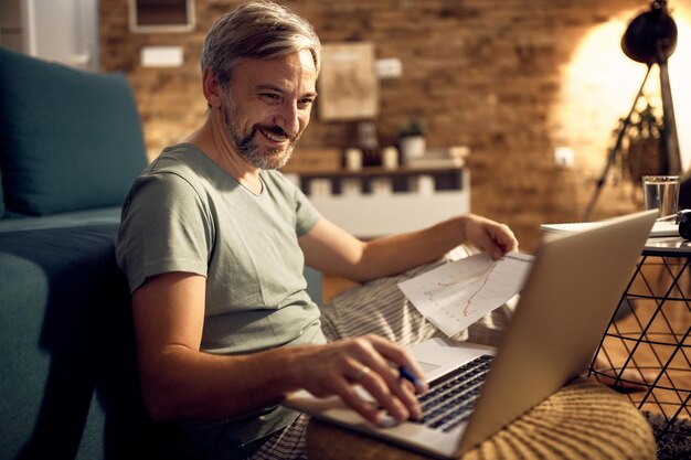 Glücklicher Unternehmer, der am Laptop arbeitet, während er nachts zu Hause Pyjamas trägt