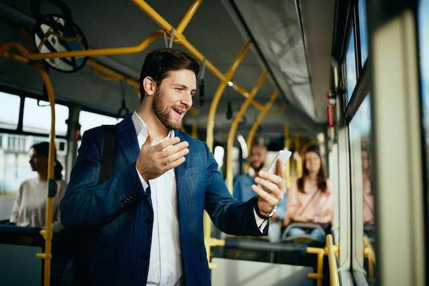 Glücklicher Unternehmer, der beim Pendeln mit dem Bus einen Videoanruf über das Handy hat