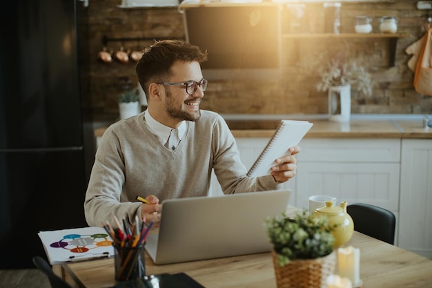 Glücklicher Unternehmer liest Notizen, während er zu Hause am Laptop arbeitet