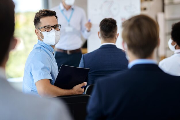 Kostenloses Foto glücklicher unternehmer mit gesichtsmaske, der an einem geschäftsseminar im sitzungssaal teilnimmt