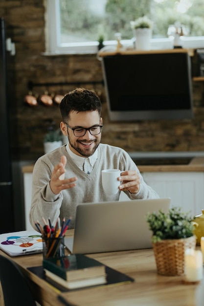 Glücklicher Unternehmer trinkt Kaffee während der Telefonkonferenz über Laptop zu Hause