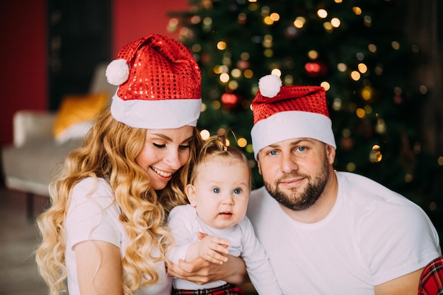 Glücklicher Vater in Weihnachtsmütze in der Nähe seiner Frau und seines Babys zu Hause