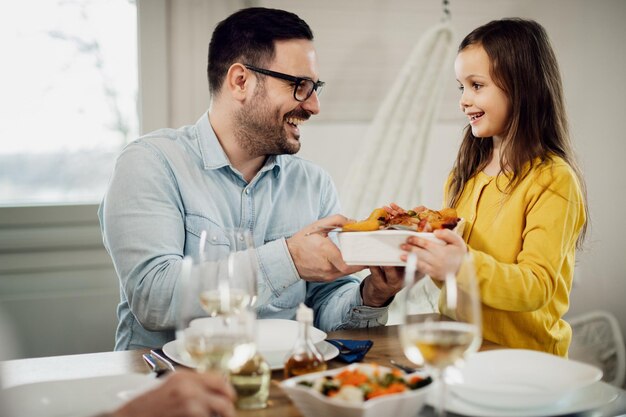 Glücklicher Vater spricht mit seiner kleinen Tochter, während sie ihm beim Mittagessen im Speisesaal Essen serviert