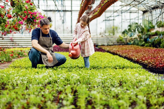 Glücklicher Vater und Tochter, die Spaß haben, während sie die Gießkanne benutzen und Blumen in der Gärtnerei nähren