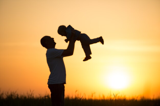 Glücklicher Vater wirft das Baby bei Sonnenuntergang