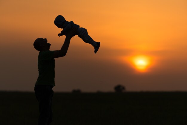Glücklicher Vater wirft das Baby bei Sonnenuntergang