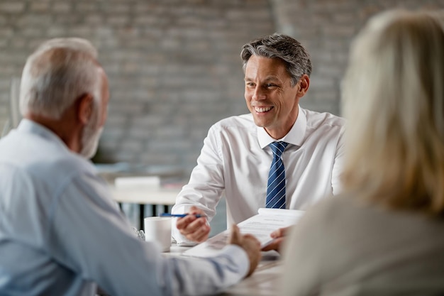 Glücklicher Versicherungsagent, der mit älteren Kunden kommuniziert, während er bei einem Meeting im Büro den Papierkram durchgeht