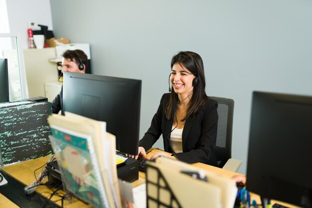 Glücklicher Vertriebsmitarbeiter, der bei der Arbeit einen großen Verkauf macht. Aufgeregte junge Frau mit Kopfhörer lacht, während sie mit einem Kunden in einem Callcenter spricht