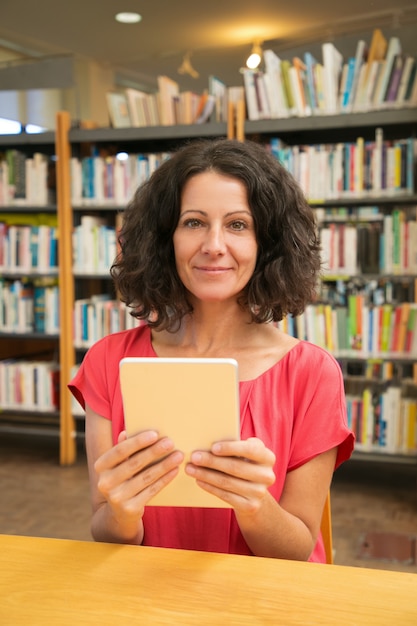 Glücklicher weiblicher Kunde mit dem Gerät, das öffentlich Bibliothek aufwirft