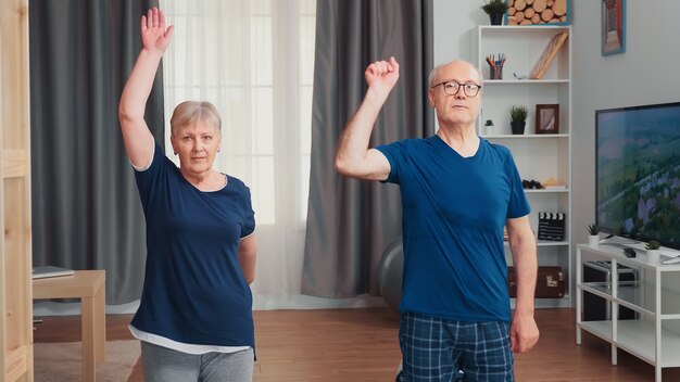 Glückliches älteres Paar, das zusammen auf Yogamatte trainiert. Gesunder und aktiver Lebensstil für ältere Menschen zu Hause, Training und Fitness für ältere Menschen