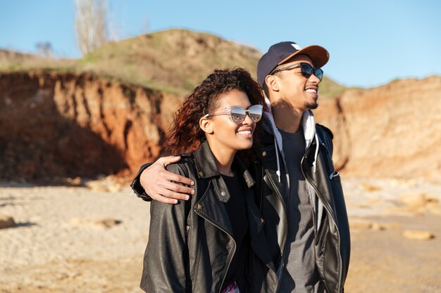 Glückliches afrikanisches liebendes Paar, das draußen am Strand geht