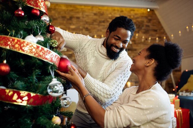 Glückliches afroamerikanisches Paar, das den Weihnachtsbaum im Wohnzimmer schmückt