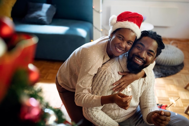 Glückliches afroamerikanisches Paar, das sich mit Wunderkerzen amüsiert, während es zu Hause Weihnachten feiert