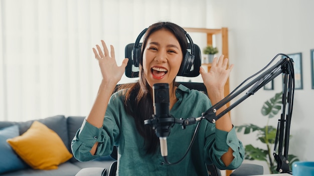 Glückliches asiatisches Mädchen, das einen Podcast mit Kopfhörern und Mikrofon aufzeichnet