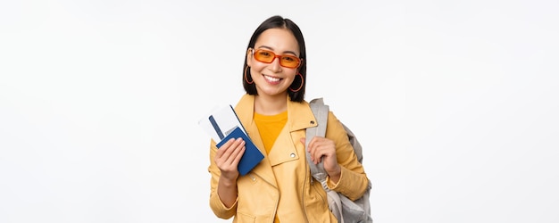 Glückliches asiatisches Mädchen, das in den Urlaub geht und Reisepass und Flugtickets Rucksack auf der Schulter hält Junge Frau Tourist, die ins Ausland reist, steht über weißem Hintergrund