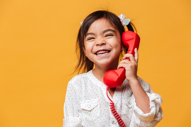 Glückliches aufgeregtes kleines Mädchen, das durch rotes Retro- Telefon spricht.