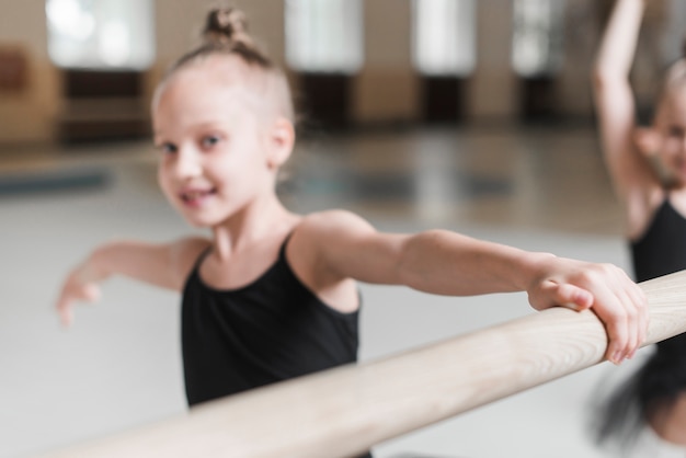 Kostenloses Foto glückliches ballerinamädchen, das auf hölzerner stange übt