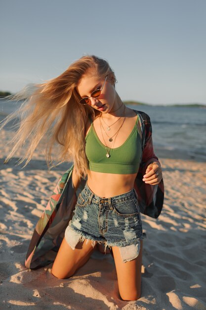 Glückliches blondes Mädchen, das am Strand aufwirft und Sommer genießt.