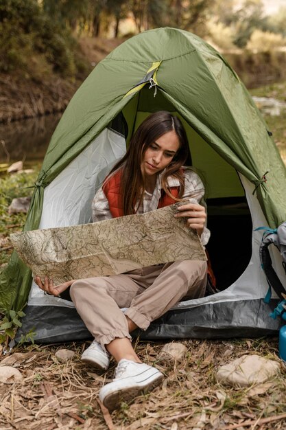 Glückliches Campingmädchen im Wald, das die Kartenvorderansicht prüft