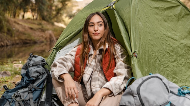 Glückliches Campingmädchen im Wald, das in der Vorderansicht des Zeltes sitzt