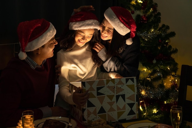 Glückliches Familienporträt, Vater, Mutter und Tochter feiern Weihnachten und Neujahr zusammen und öffnen eine Geschenkbox mit magischer Überraschung