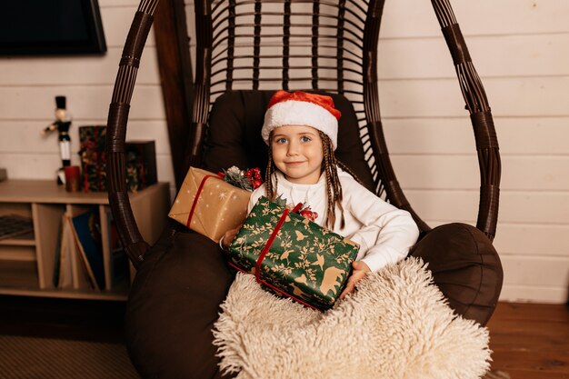 Glückliches freudiges kleines Mädchen, das Weihnachtsmütze trägt, der mit Weihnachtsgeschenken aufwirft