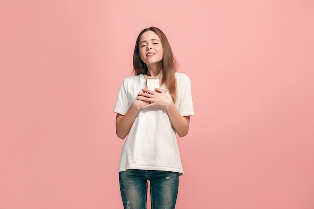 Glückliches jugendlich Mädchen stehend, lächelnd mit Handy über trendigem rosa Studio