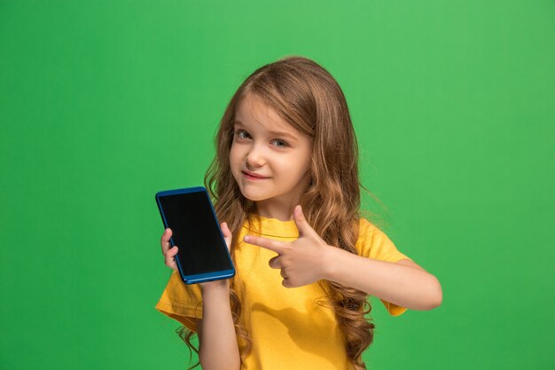 Glückliches jugendlich Mädchen stehend, lächelnd mit Handy über trendiger grüner Studiowand