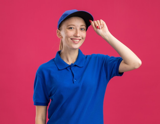 Glückliches junges Liefermädchen in blauer Uniform und Mütze, das zuversichtlich lächelt