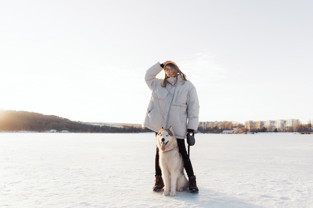 Glückliches junges Mädchen, das mit Siberian Husky Hund im Winterpark spielt