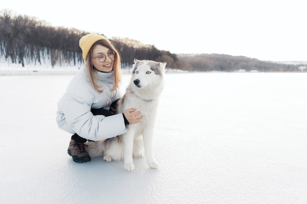 Glückliches junges Mädchen, das mit Siberian Husky Hund im Winterpark spielt